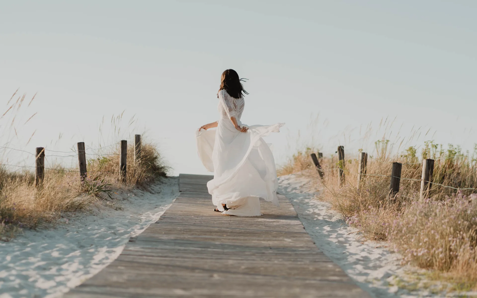 Novia caminando por una pasarela de madera entre las dunas