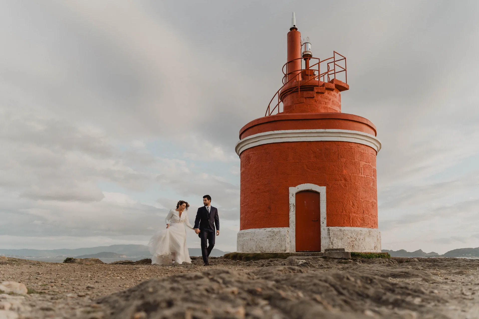 Novios junto a un faro rojo en la costa